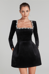 Elegant black velvet Christmas party dress with jeweled square neckline, long sleeves, and A-line skirt, modeled against a studio backdrop