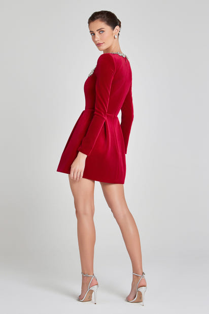 Elegant red velvet Christmas dress with jewelled square neckline, long sleeves, and flared mini skirt, modelled from the back in festive holiday setting.