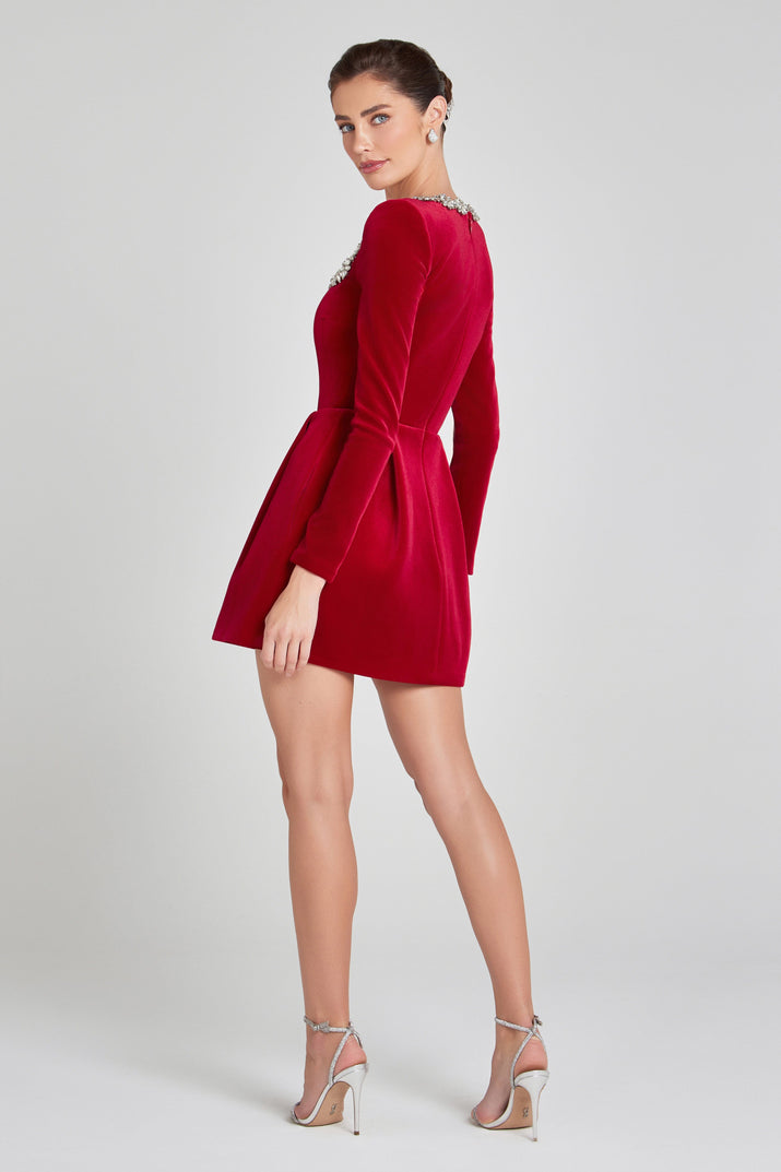 Elegant red velvet Christmas dress with jewelled square neckline, long sleeves, and flared mini skirt, modelled from the back in festive holiday setting.